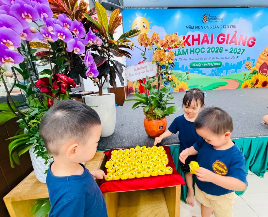 Ba bạn nhỏ FBK chọn quà từ khay nhung đỏ bên cạnh chậu lan chúc mừng
