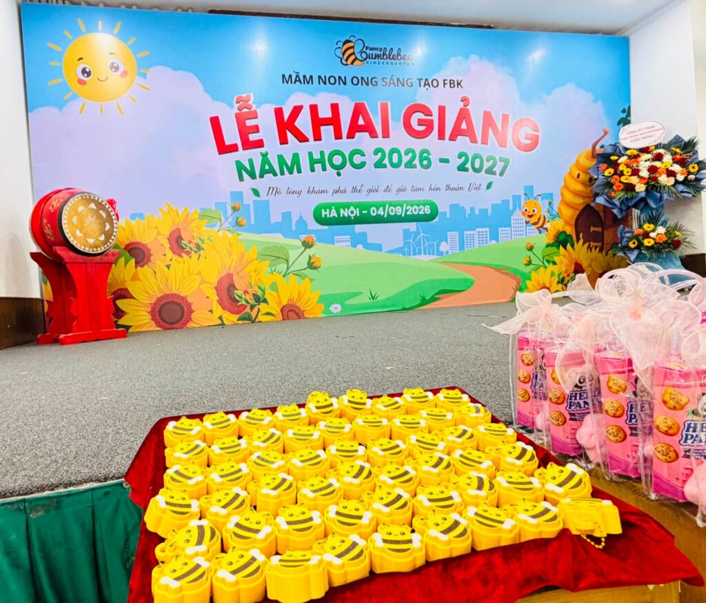 Sân khấu lễ khai giảng FBK với phông hoa hướng dương, trống khai giảng và khay quà hình con ong